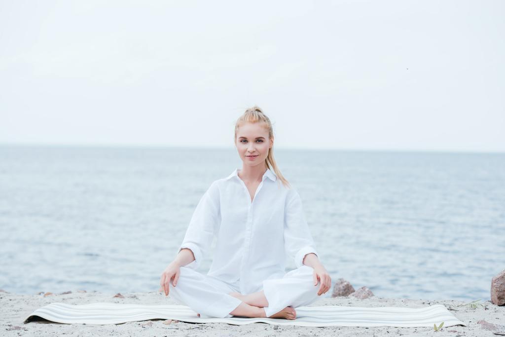 glückliche und schöne blonde junge Frau praktiziert Yoga in der Nähe des Flusses  - Foto, Bild