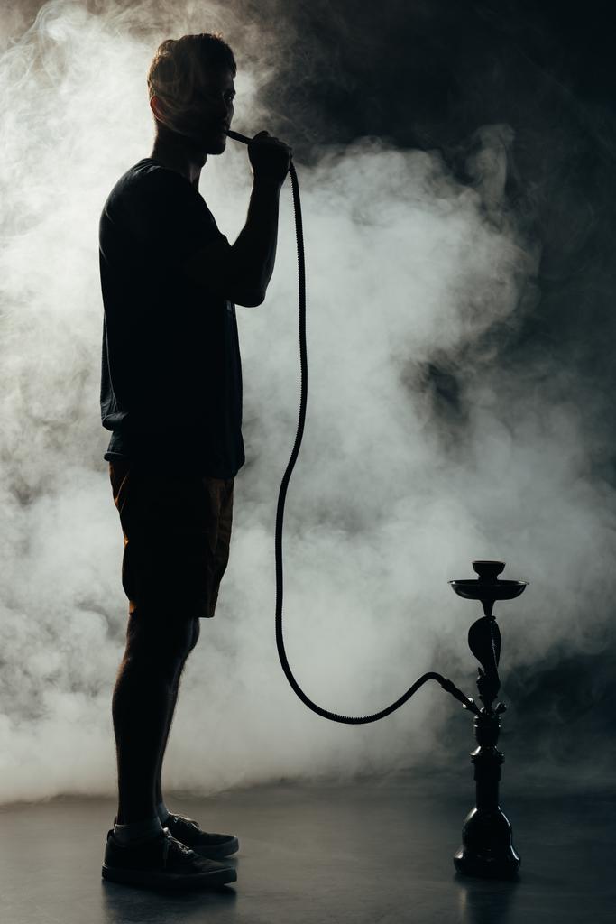 volledige lengte weergave van silhouet roken waterpijp in duisternis - Foto, afbeelding