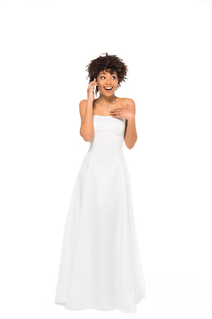 興奮したアフリカ系アメリカ人の花嫁が立って、白で孤立したスマートフォンで話す  - 写真・画像