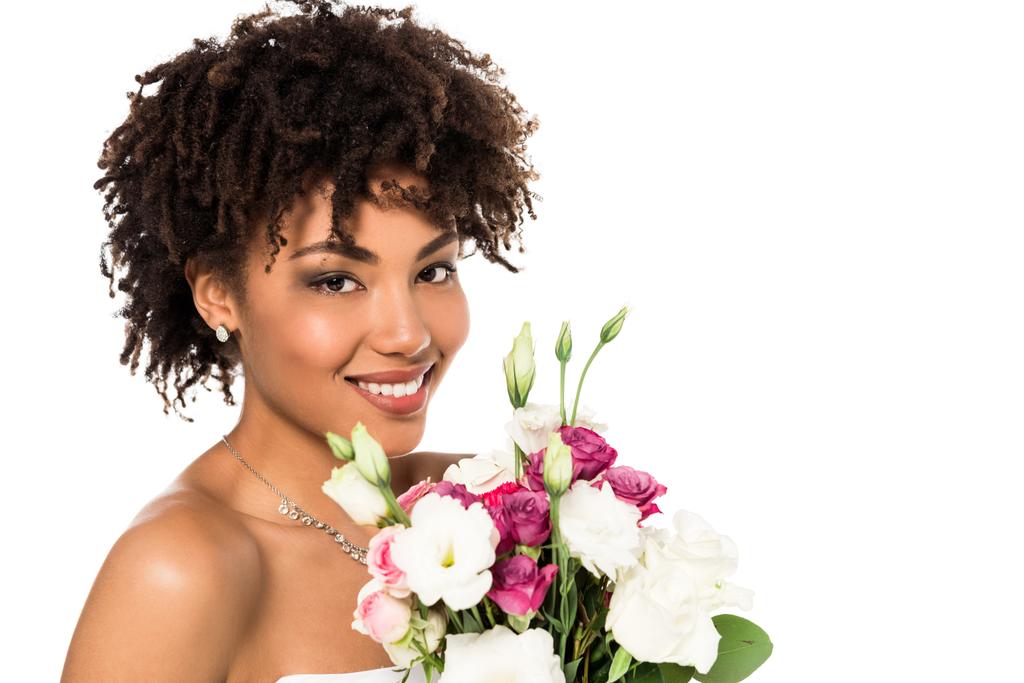 felice ragazza africana americana in abito da sposa in possesso di bouquet e guardando la fotocamera isolata su bianco
  - Foto, immagini