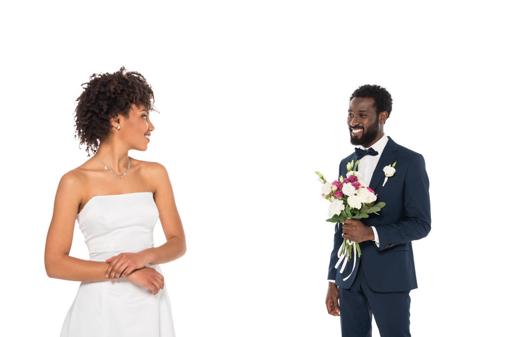 白で孤立した幸せなアフリカ系アメリカ人の花嫁の近くに花を持つひげの花婿の選択的な焦点 - 写真・画像
