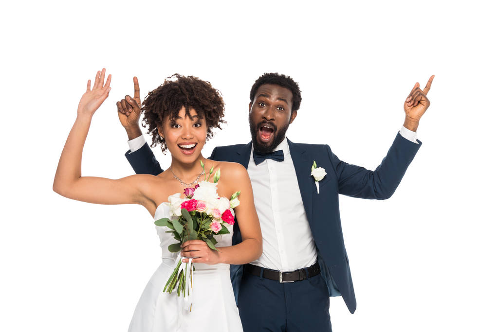 花婿とジェスチャーで立っている幸せなアフリカ系アメリカ人の花嫁は、白に隔離された花を保持しながら - 写真・画像