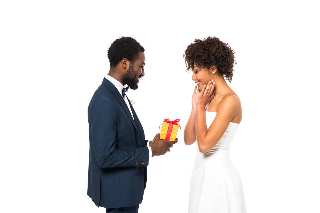 šťastný afroamerický ženich, který dává dar veselé nevěstě osamocen na bílém  - Fotografie, Obrázek