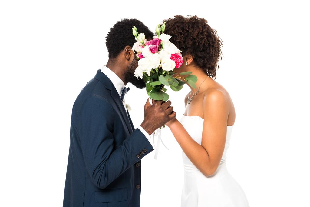 africká americká nevěsta a ženich zakrývající obličeje a držením květin izolovaných na bílém  - Fotografie, Obrázek