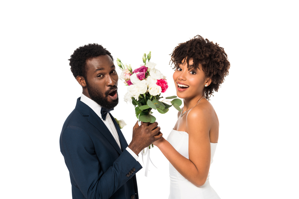 surprised african american bridegroom and happy bride holding flowers isolated on white  - Photo, Image