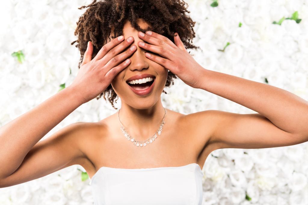 noiva americana africana alegre cobrindo olhos com as mãos perto de flores
  - Foto, Imagem