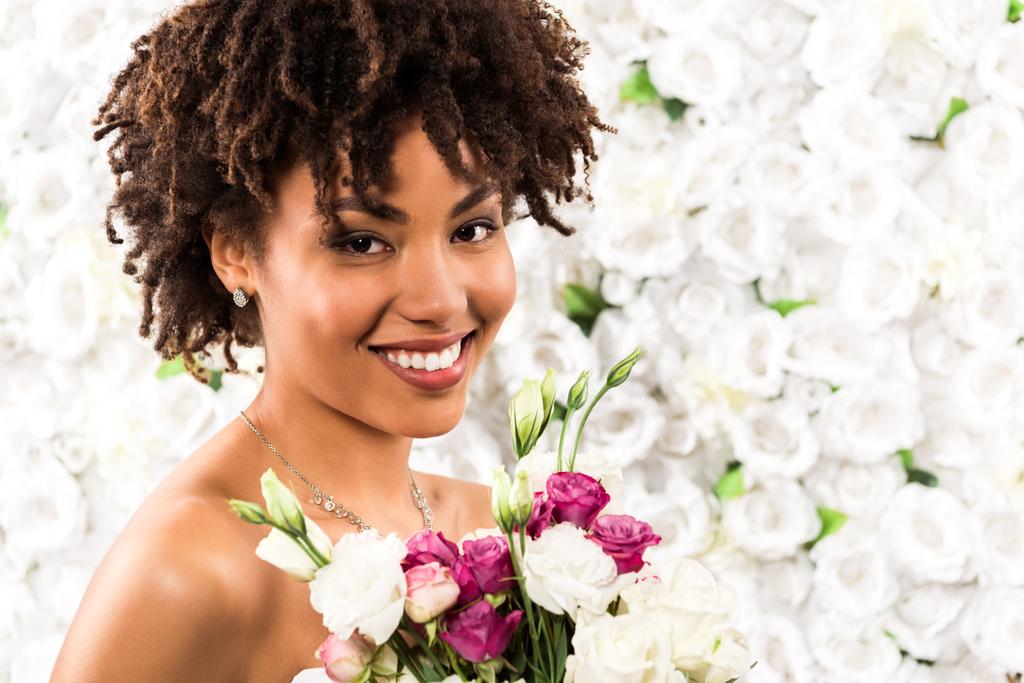 花を持ちながらカメラを見て微笑むアフリカ系アメリカ人の花嫁  - 写真・画像