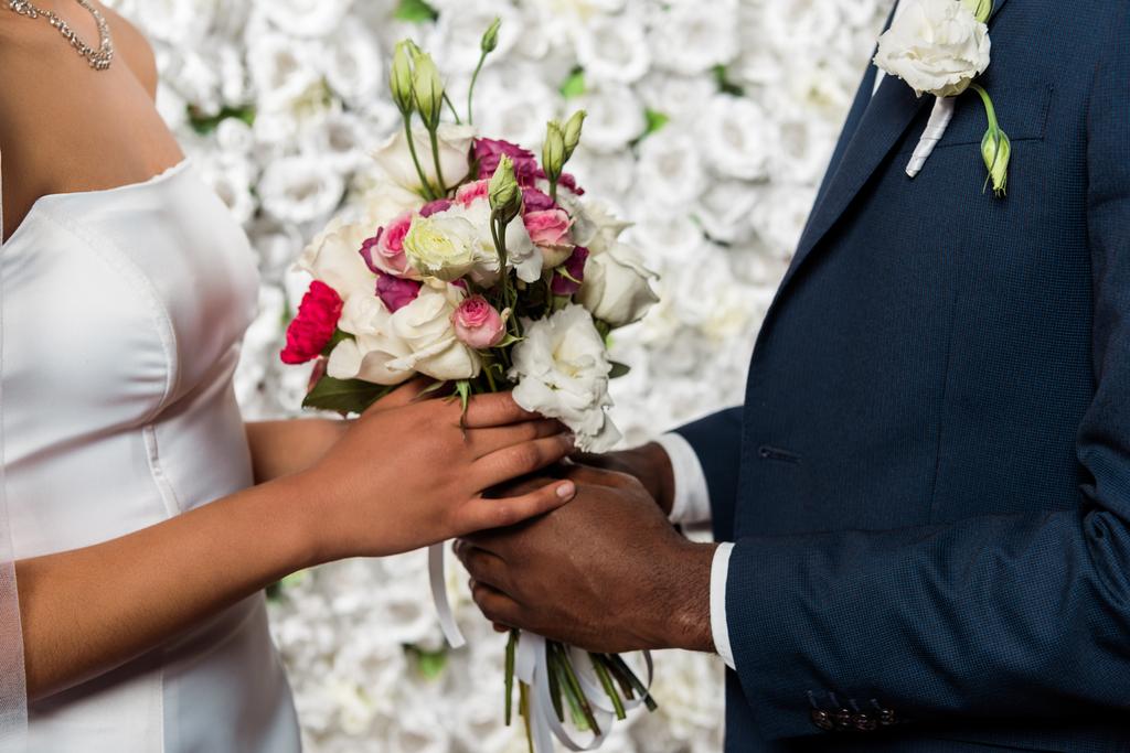 κομμένη θέα του Αφρικανός Αμερικανός γαμπρός και νύφη κρατώντας λουλούδια  - Φωτογραφία, εικόνα