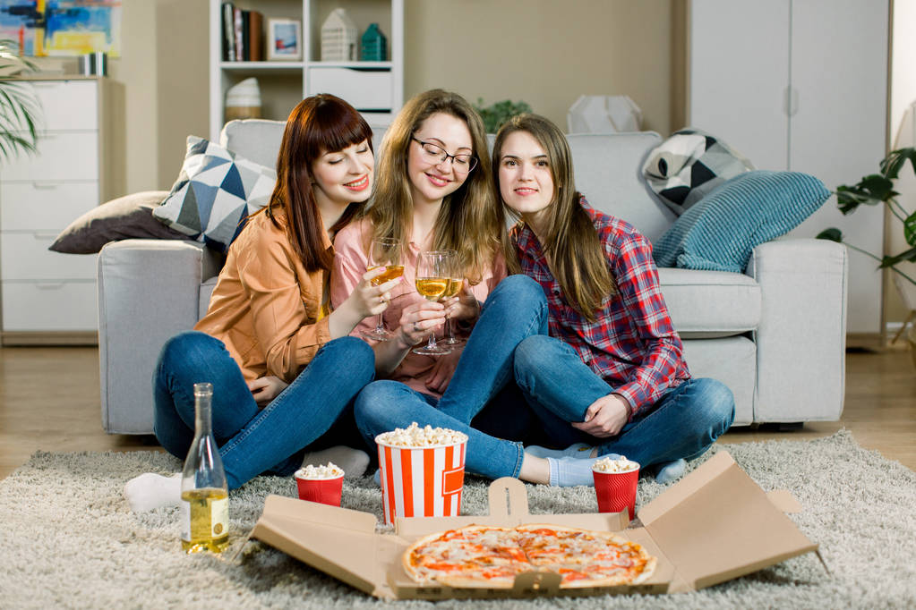 Специальное мероприятие. Служба доставки быстрого питания. Три девушки в повседневной одежде едят вкусную пиццу, попкорн и пьют вино на их модной вечеринке
. - Фото, изображение