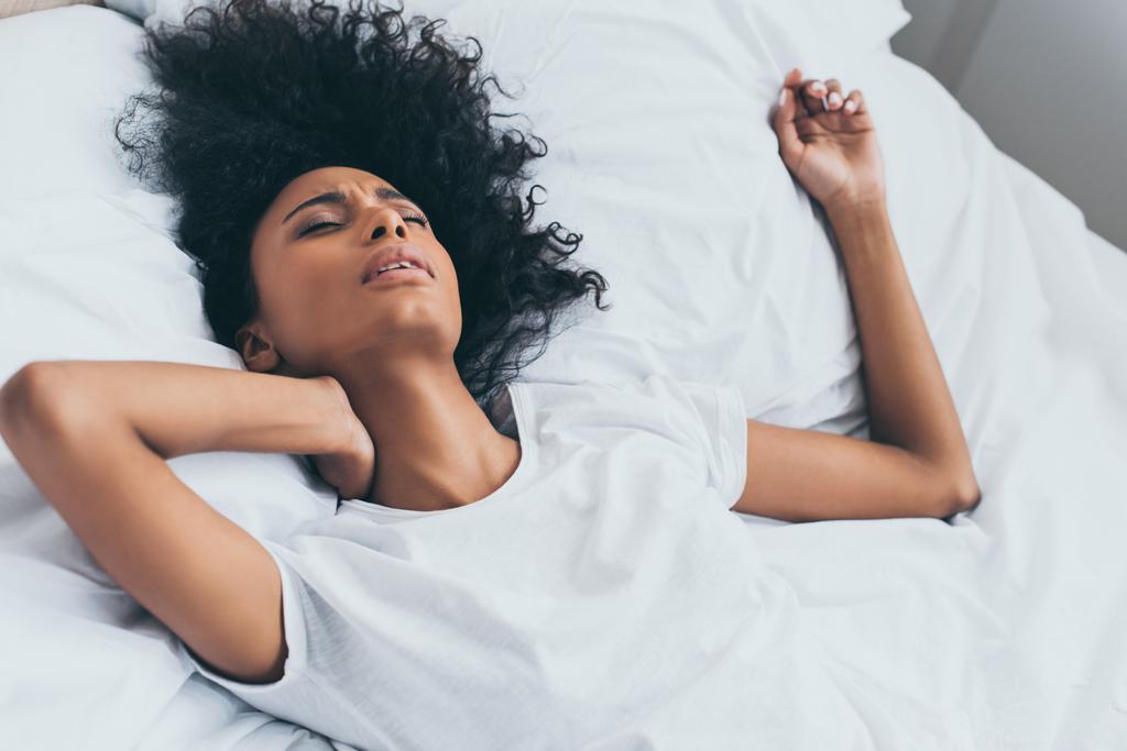 bella donna afro-americana che soffre di dolore al collo mentre si trova a letto
 - Foto, immagini