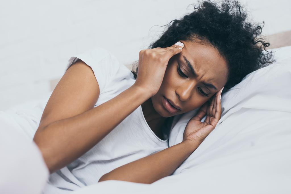 ベッドに横たわっている間に頭痛に苦しむかなりアフリカ系アメリカ人女性 - 写真・画像