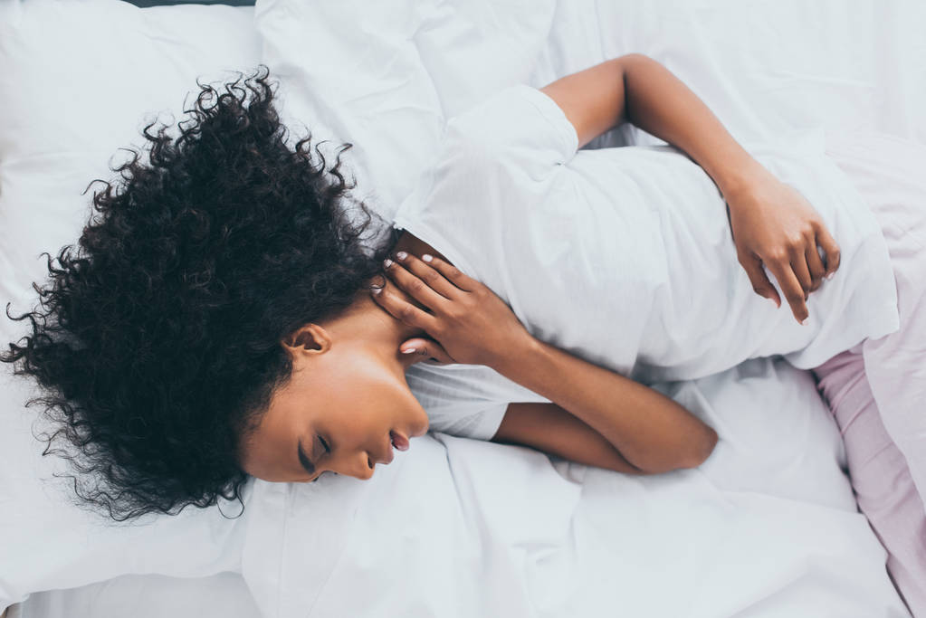 exhausted african american woman suffering from pain in neck while lying in bed - Photo, Image