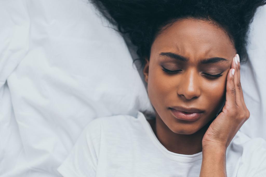 Widok z góry całkiem African American kobieta cierpi na ból głowy, leżąc w łóżku - Zdjęcie, obraz