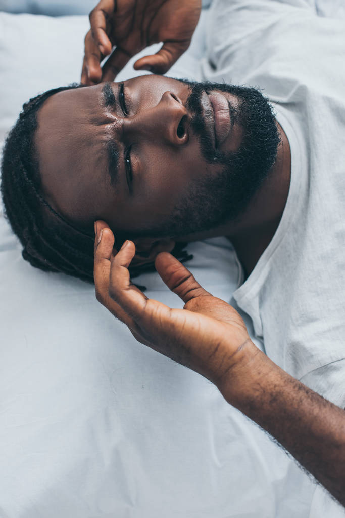 ベッドに横たわっている間に頭痛に苦しむ不幸なアフリカの男性 - 写真・画像