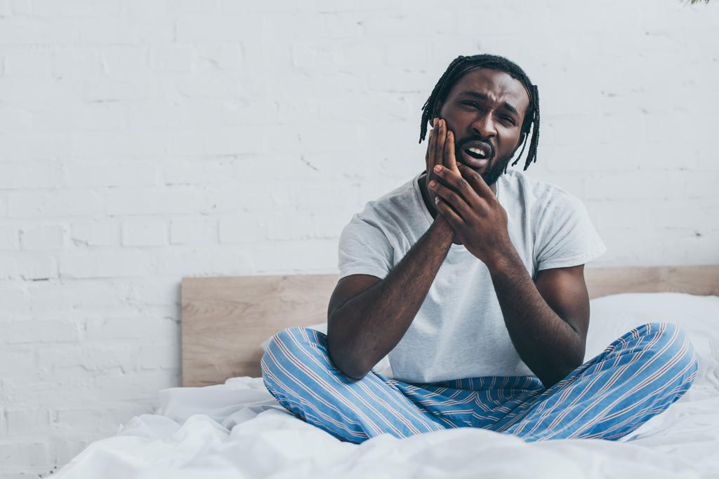 寝室で歯の痛みに苦しむパジャマのハンサムなアフリカ系アメリカ人男性 - 写真・画像