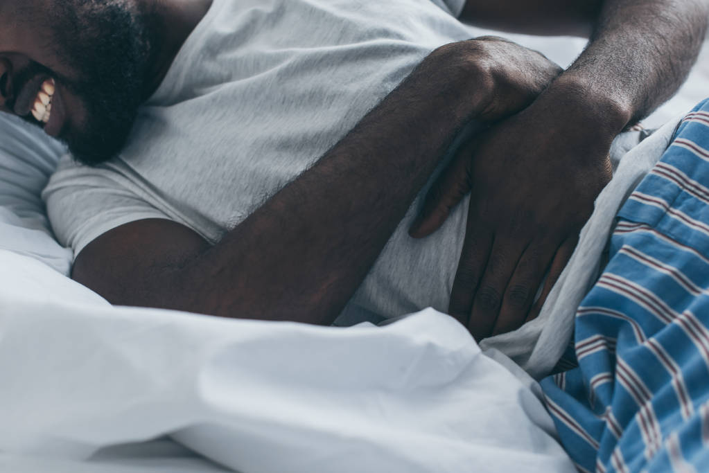 μερική θέα του αφρικανικού Αμερικάνικου ανθρώπου που πάσχει από κοιλιακό άλγος στο υπνοδωμάτιο - Φωτογραφία, εικόνα