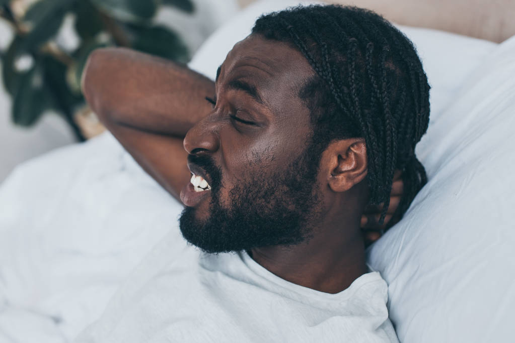 unglücklicher afrikanisch-amerikanischer Mann leidet unter Nackenschmerzen im Bett - Foto, Bild