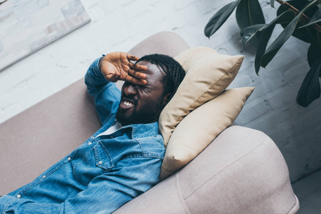 esausto uomo afroamericano sdraiato sul divano e affetto da mal di testa
 - Foto, immagini