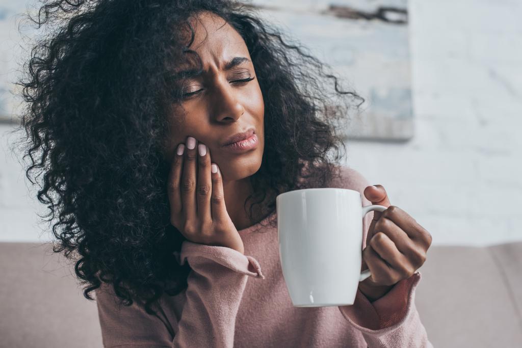 unglückliche afrikanisch-amerikanische Frau leidet unter Zahnschmerzen und hält Kaffeetasse - Foto, Bild