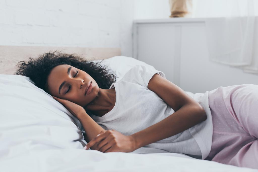 mooie Afrikaanse Amerikaanse vrouw in pyjama slapen op wit beddengoed - Foto, afbeelding