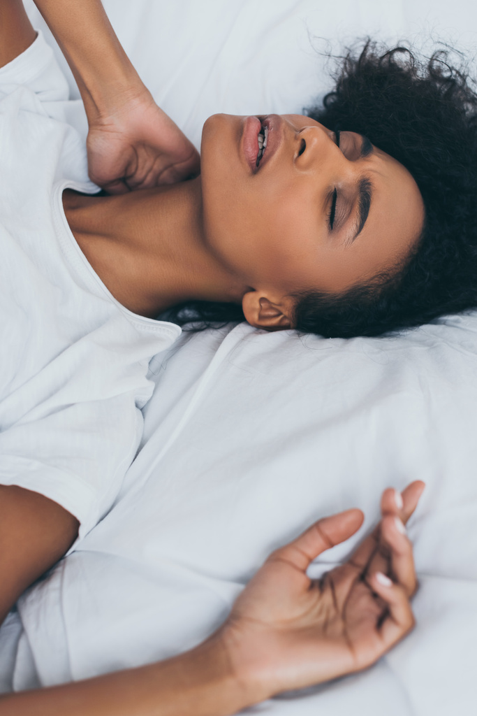 目を閉じてベッドに横たわっている間、首の痛みに苦しむ疲れ果てたアフリカ系アメリカ人女性 - 写真・画像