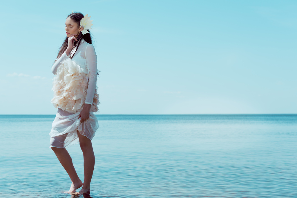 白鳥の衣装で目を閉じるブルネットの女性,川と空の背景に立つ  - 写真・画像
