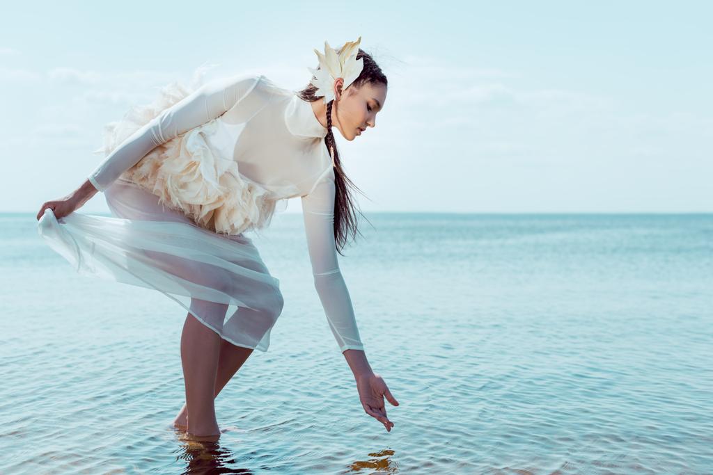 femme adulte en costume de cygne blanc touchant l'eau, regardant la rivière
 - Photo, image