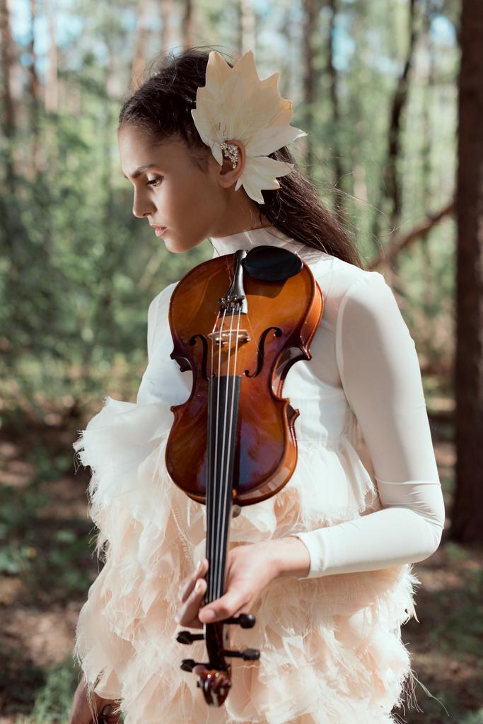 tarjouksen nainen valkoisessa joutsen puku seisoo metsässä taustalla viulu, katselee pois
 - Valokuva, kuva
