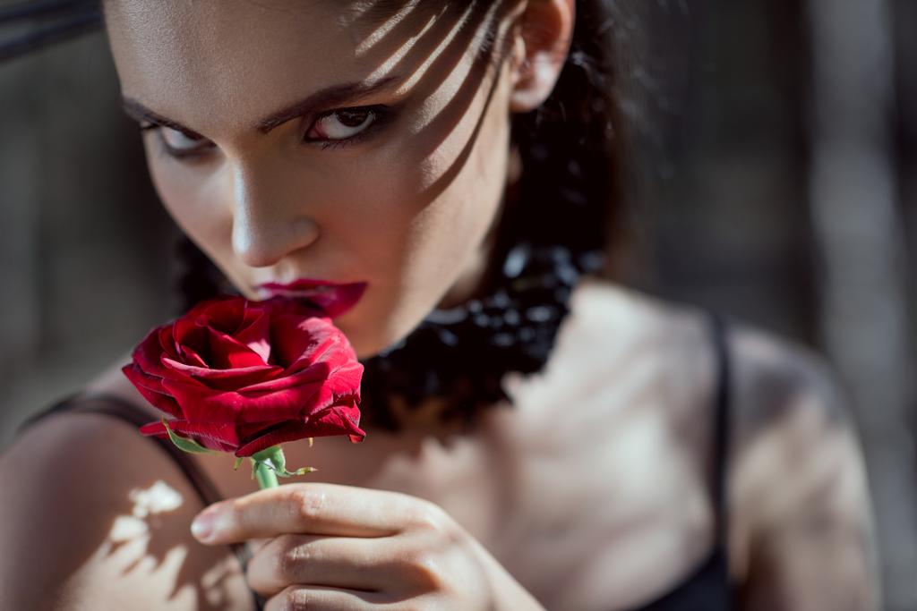 portrét nádherné ženy v černém kostýmu s červenou růží v ruce, pohled na kameru - Fotografie, Obrázek