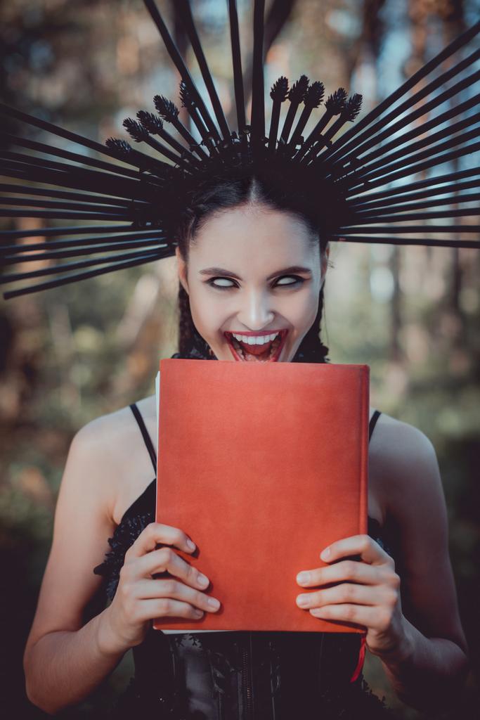 頭に王冠を持つ黒い魔女の衣装を着た狂った女性 赤い本を持つ ロイヤリティフリー写真 画像素材