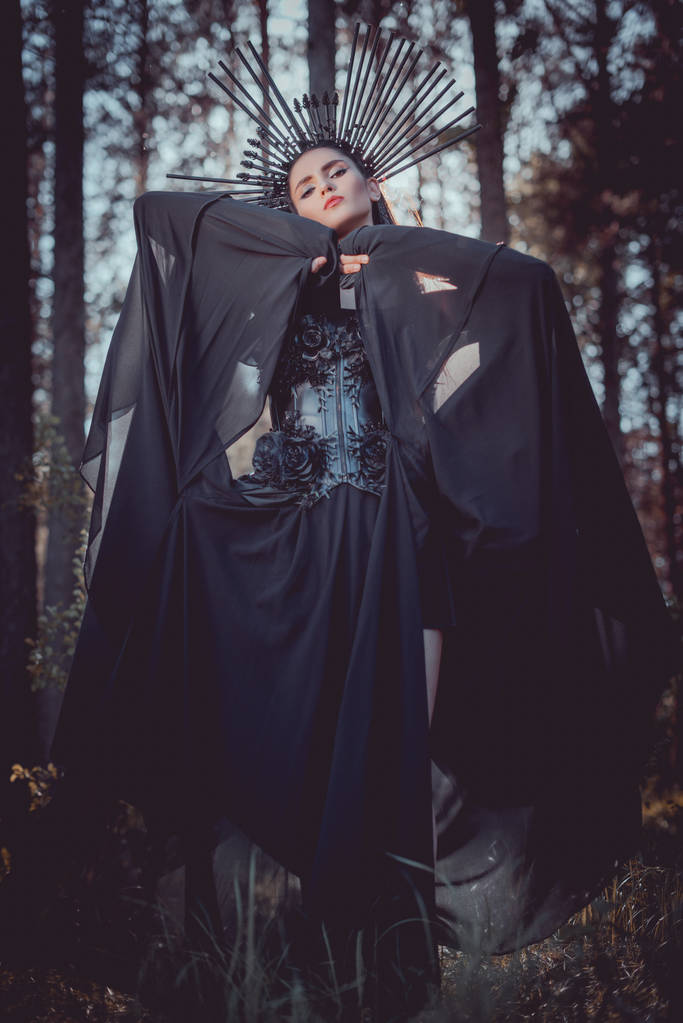 alacsony szögben véve a nő a boszorkány jelmez és a koronát a fej kézfogást fekete textil az arc közelében - Fotó, kép