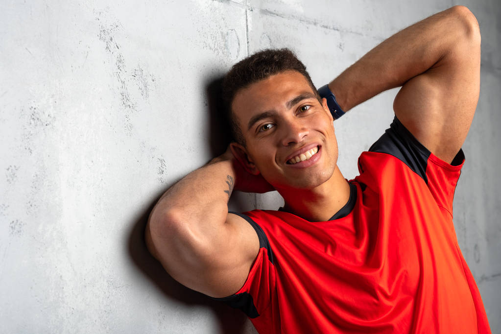 Jovem desportivo homem em vermelho t-shirt posando no fundo de concreto cinza
  - Foto, Imagem