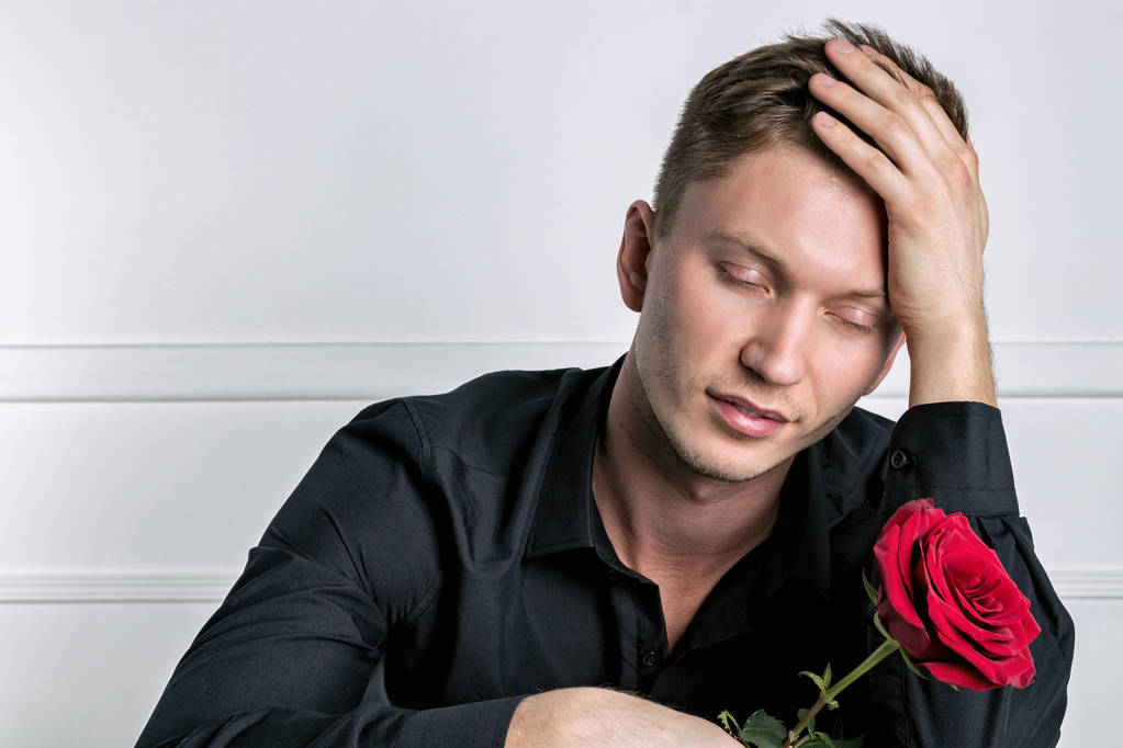 Bonito homem vestindo camisa preta segurando uma rosa e se preparando encontro romântico
 - Foto, Imagem