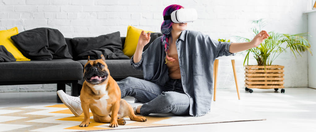 панорамный снимок девушки с красочными волосами и VR гарнитурой, сидящей на полу рядом с собакой
 - Фото, изображение