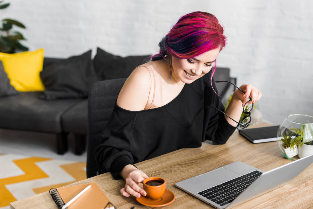 csípő lány színes haj ülés mögött asztal, mosolygós és használata laptop - Fotó, kép