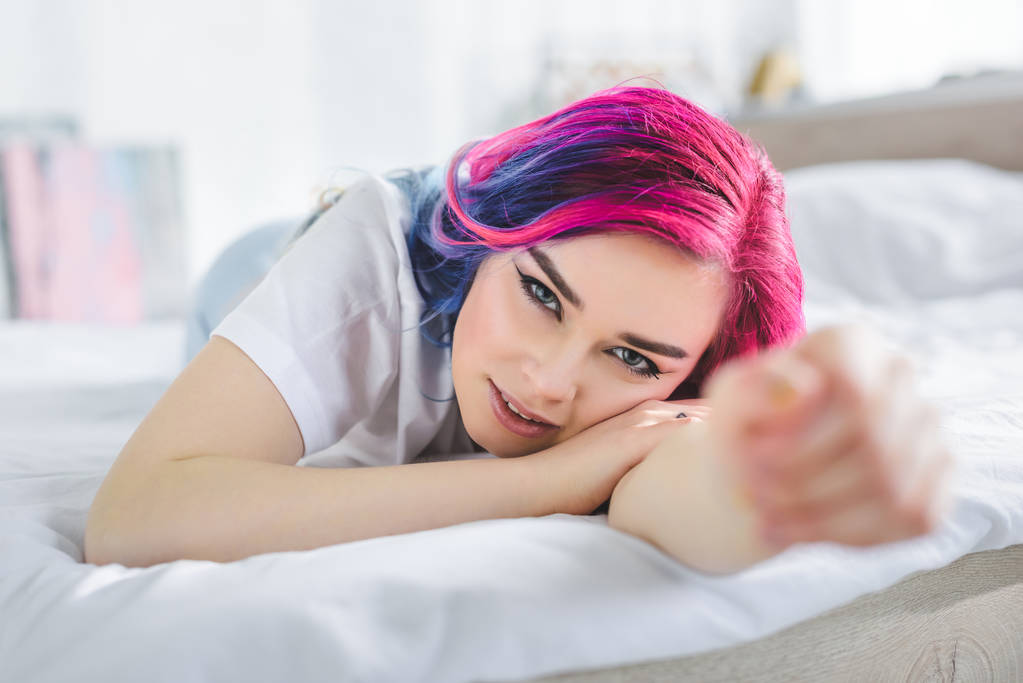 selektywne skupienie pięknej dziewczyny z kolorowymi włosami układania w łóżku i patrząc na kamerę  - Zdjęcie, obraz