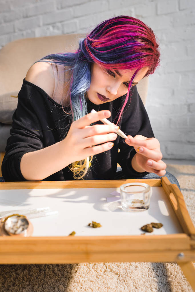 gericht mooi meisje maken joint met medische marihuana terwijl zittend op de vloer achter de tafel  - Foto, afbeelding