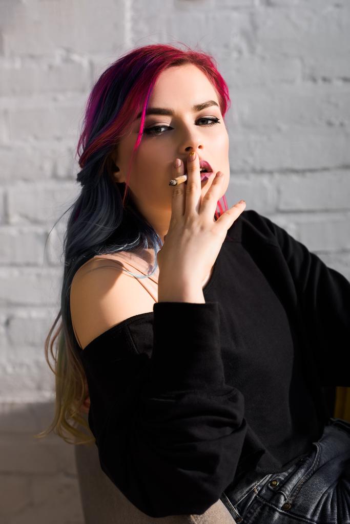 krásná dívka s pestrobarevné vlasy, sedící v křesle, kouřící a pohled na kameru  - Fotografie, Obrázek