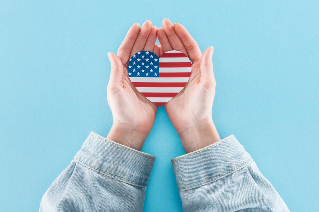 μερική θέα της γυναίκας που κρατά την καρδιά από την εθνική αμερικανική σημαία σε μπλε φόντο - Φωτογραφία, εικόνα