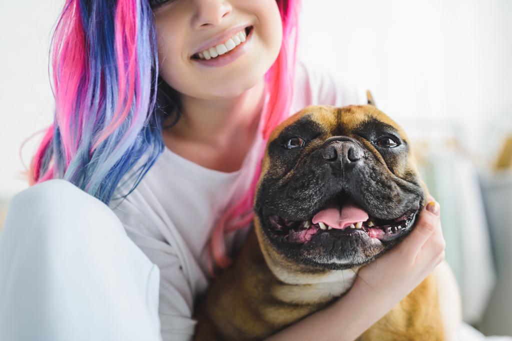 περικομμένη όψη του ευτυχισμένο κορίτσι με πολύχρωμα μαλλιά αγκάλιασμα χαριτωμένο μπουλντόγκ - Φωτογραφία, εικόνα