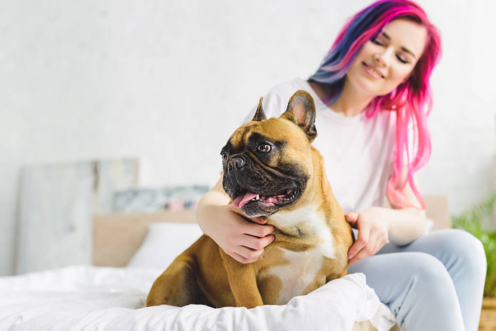 selective focus of girl sitting on bed and petting cute bulldog looking away - Photo, Image