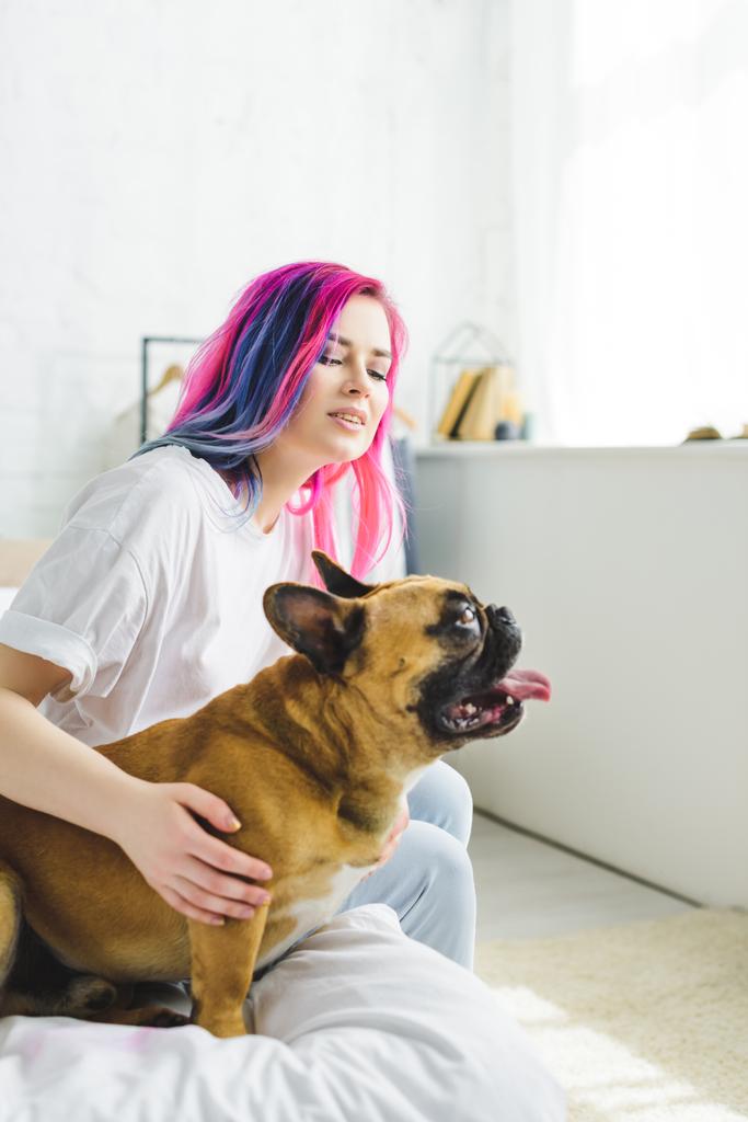 yatakta otururken uzağa bakan renkli saç petting bulldog ile kız  - Fotoğraf, Görsel