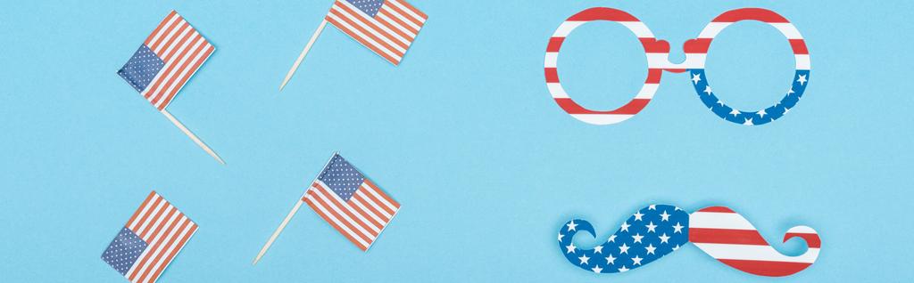 mavi arka plan üzerinde ahşap çubuklar üzerinde dekoratif Amerikan bayrakları yakınında yıldız ve çizgili yapılmış gözlük ve bıyık panoramik çekim - Fotoğraf, Görsel
