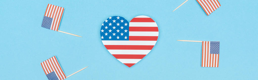 panoramic shot of heart made of stars and stripes near decorative american flags on wooden sticks on blue background - Photo, Image