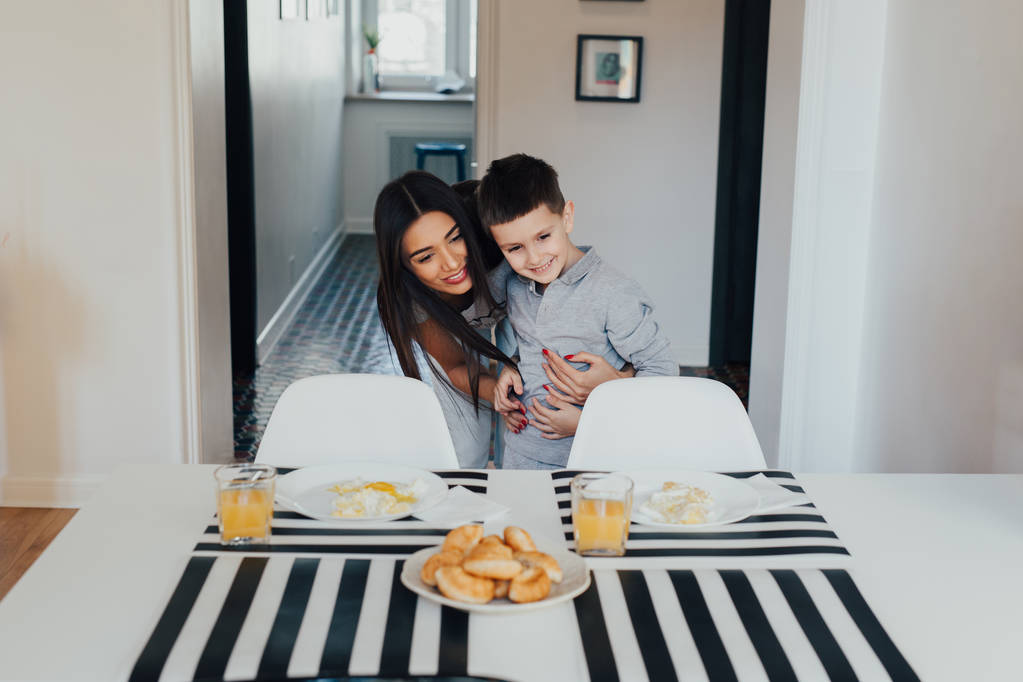 Beautiful young woman at home with her little cute son are having breakfast together - Photo, Image