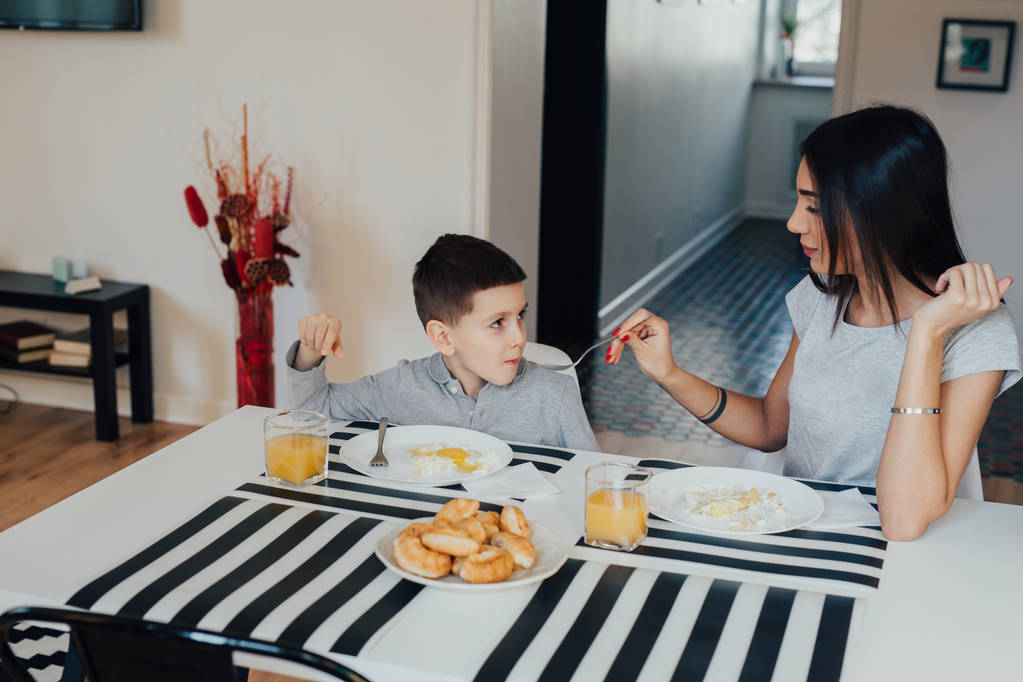 Beautiful young woman at home with her little cute son are having breakfast - Photo, Image