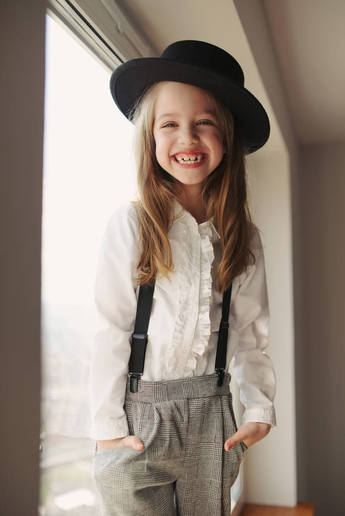 schattig klein meisje met zwarte hoed thuis - Foto, afbeelding