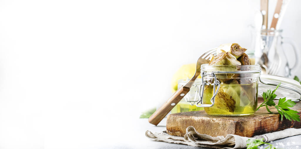 Carciofi in olio d'oliva in vaso con limone ed erbe aromatiche su sfondo grigio tavolo da cucina, focus selettivo
 - Foto, immagini