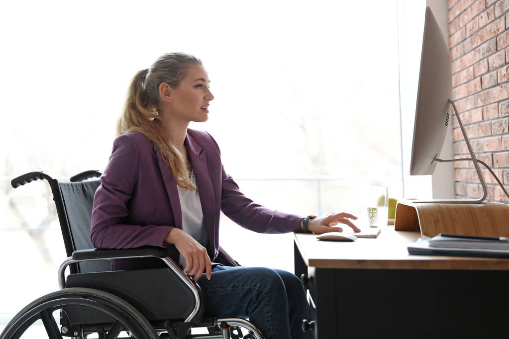 Žena na invalidním vozíku pracuje s počítačem u stolu uvnitř - Fotografie, Obrázek