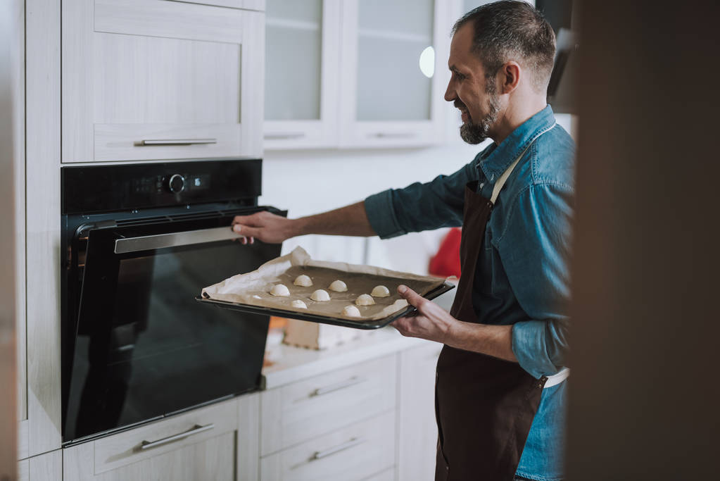 Lachende man Holding Sheet pan en openen van de oven - Foto, afbeelding